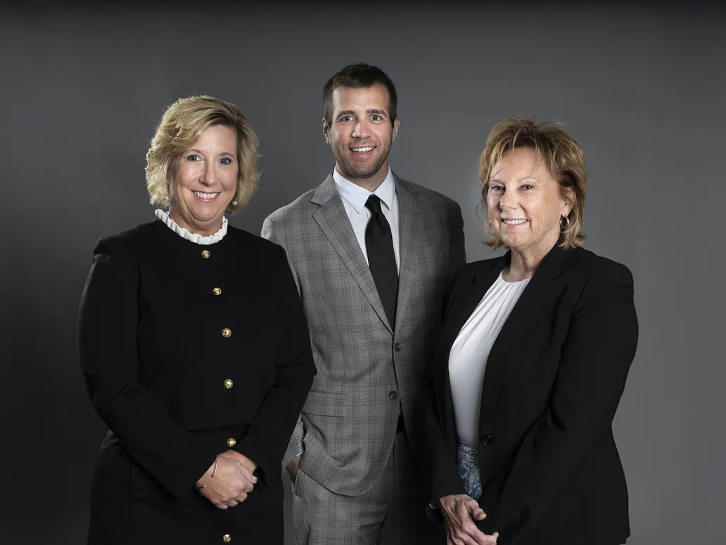 Three business professionals smiling together for a group photo in a corporate setting