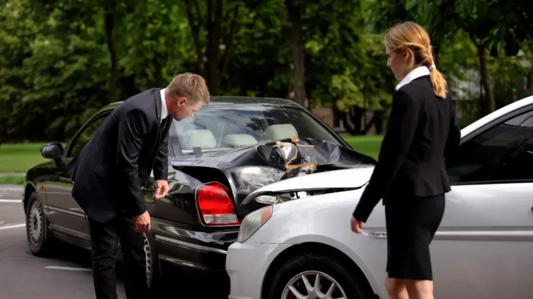 Two professionally dressed individuals inspecting damage after a black car rear-ended a white car.